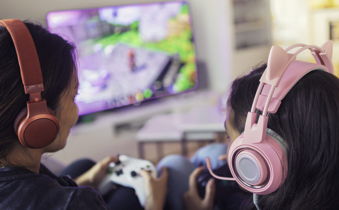 Close up of a mother and daughter playing video games together on a video game console using gamepads and headsets.