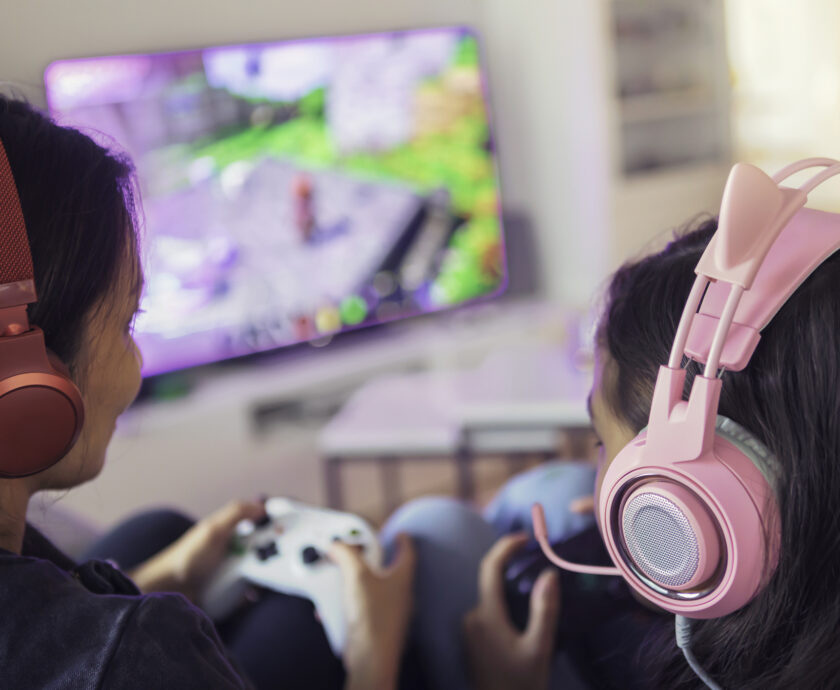 Close up of a mother and daughter playing video games together on a video game console using gamepads and headsets.