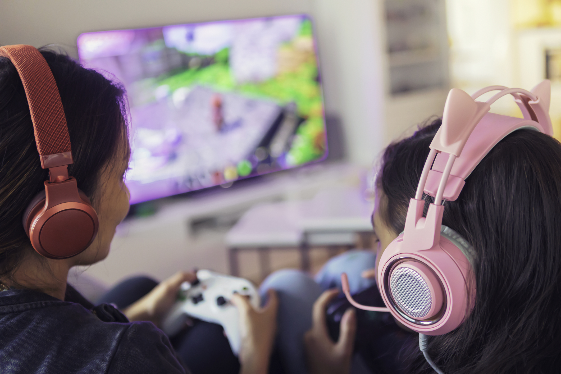 Close up of a mother and daughter playing video games together on a video game console using gamepads and headsets.