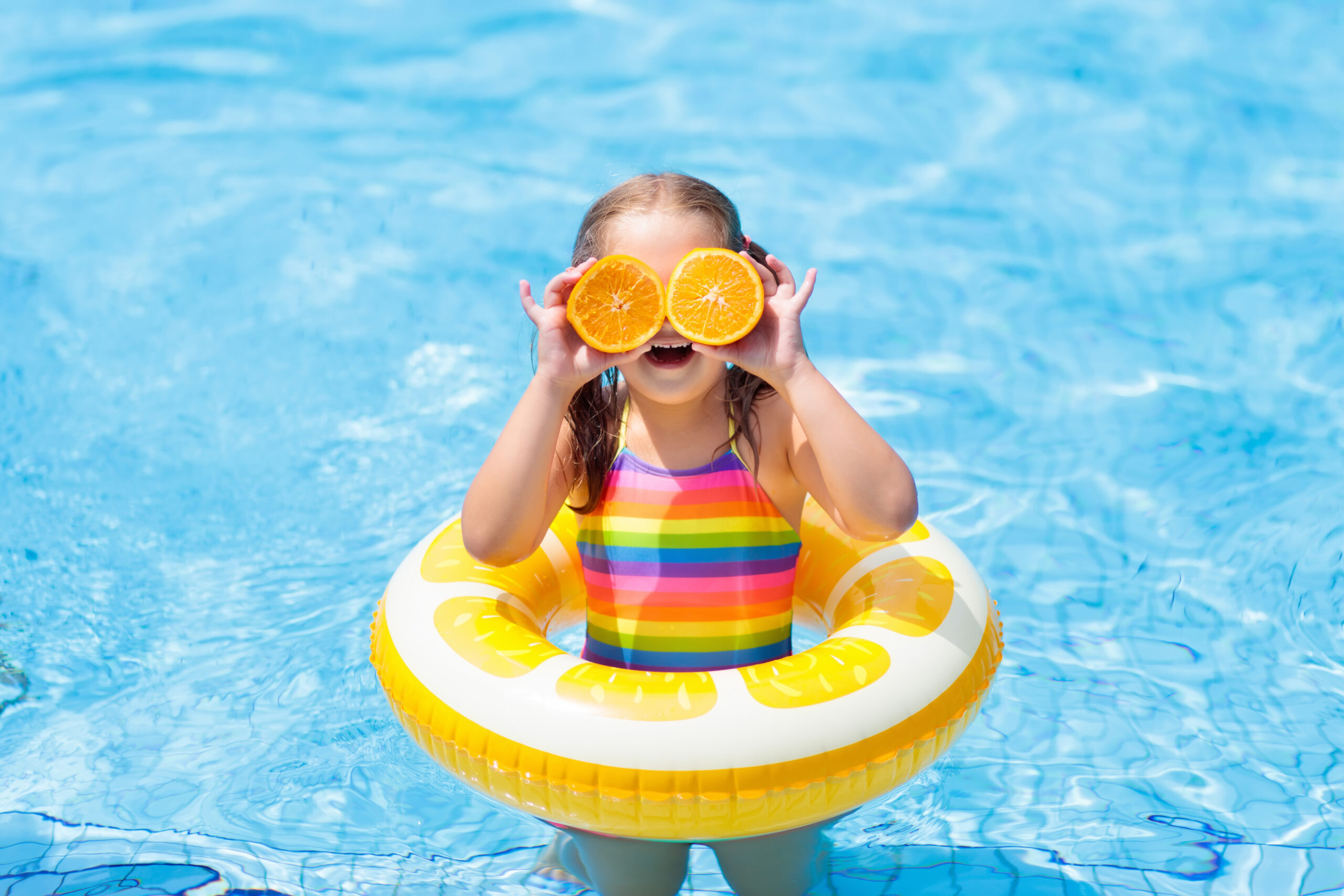Little girl in swimming pool with inflatable toy ring eating orange. Kids swim on summer vacation. Tropical fruit and healthy snack. Swim aids for child. Kid on colorful float. Beach and water fun.